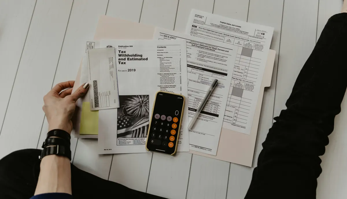 A person working through figures on paper with a pen and calculator